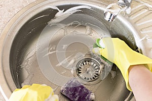 Woman in yellow rubber gloves washes and cleans a sink with a sponge and brush.
