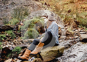 Woman in yellow shirt and hat sitting on stone in strem  in the autumn forest photo