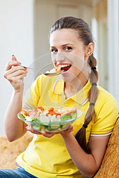 Woman eating vegetables salad on sofa