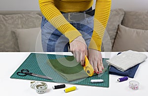 Woman in a yellow sweater cuts the fabric. there are quilting tools on the table. patchwork knife, scissors, lined cutting mat,