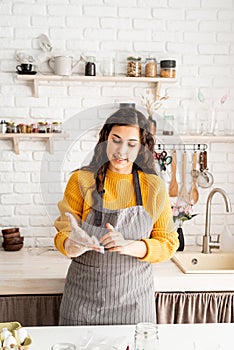 Woman in yellow sweater and gray apron preparing to color easter eggs in the kitchen putting on the gloves