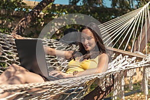 A woman in a yellow swimsuit lying in a hammock using a laptop