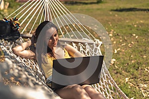 A woman in a yellow swimsuit lying in a hammock using a laptop