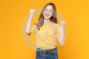 Woman in a yellow t-shirt raises arms and fists clenched with shows strong powerful, celebrating victory expressing success.