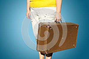 Woman in a yellow T-shirt stands with a suitcase in her hand