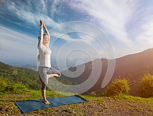 Woman in yoga asana Vrikshasana tree pose in mountains outdoors