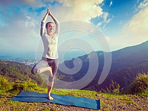 Woman in yoga asana Vrikshasana tree pose in mountains outdoors