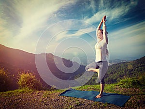 Woman in yoga asana Vrikshasana tree pose in mountains outdoors