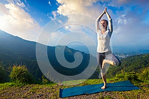 Woman in yoga asana Vrikshasana tree pose in mountains outdoors photo