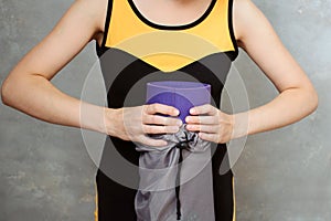 Woman yoga folds the mat into a bag, holding it with two hands. against the background of a gray plaster wall