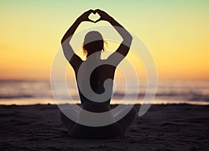 Woman yoga, heart hand and shadow at sunset at beach and ocean with peace and zen hands sign. Silhouette, nature and sea