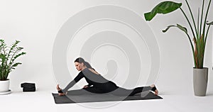 Woman yoga instructor performs forward bend in Hanumanasana, training in a sporty black long-sleeved jumpsuit