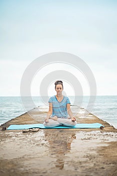 Woman yoga instructor sitting in lotus posture hands mudra admiring sea coastline landscape