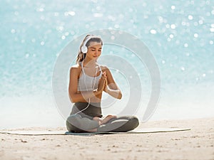 Woman in Yoga Meditation Pose with Headphones on the Beach