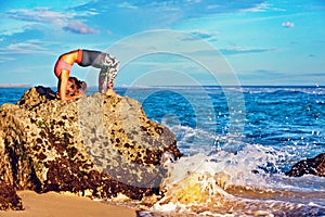 Woman in yoga pose on sea beach rock