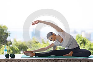 Woman, yoga and stretching body with mat by window for workout, exercise or outdoor training at home. Young female