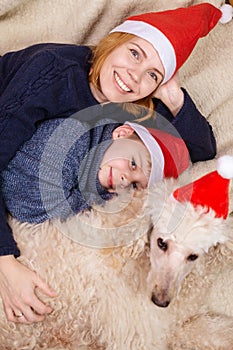 A woman with a young boy son and a dog dressed in New Year`s hats is lying on the couch and smiling