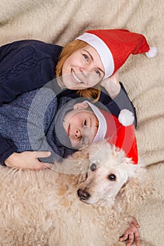 A woman with a young boy son and a dog dressed in New Year's hats is lying on the couch and smiling