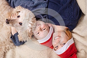 A woman with a young boy son and a dog dressed in New Year's hats is lying on the couch and smiling. View from above