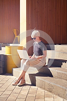 Woman young entrepreneur with short hair working on laptop, screen space for design layout. Sitting outside in cafe, feel happy.