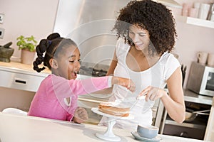 Woman and young girl in kitchen icing a cake smili