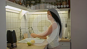 Woman young housewife washing fresh fruits in kitchen under water stream, preparation fruit salad