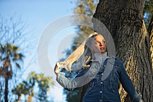 Woman, young, pretty, blonde, with blue eyes and denim dress, seen from below, touching her hair flirtatiously and looking to