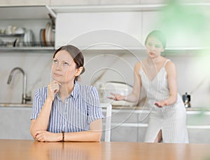 Woman and young woman in casual clothes during family quarrel in kitchen