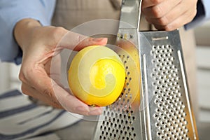 Woman zesting fresh lemon indoors, closeup view