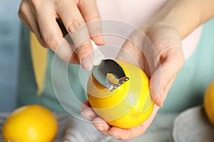 Woman zesting fresh lemon indoors, closeup view