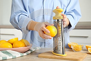 Woman zesting lemon at table indoors, closeup