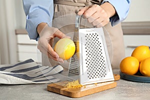 Woman zesting lemon at table indoors, closeup