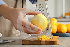 Woman zesting lemon at table indoors, closeup