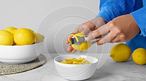 Woman zesting lemon at white marble table, closeup