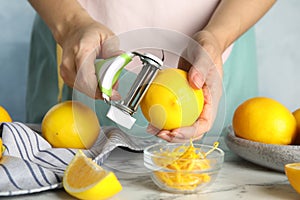 Woman zesting lemon at white marble table, closeup