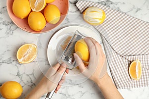 Woman zesting lemon at white marble table, top view