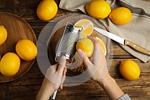 Woman zesting lemon at wooden table, top view