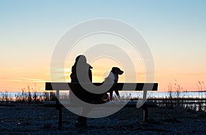 Womana and dog sitting on bench near sunset seacoast
