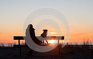 Womana and dog sitting on bench near sunset seacoast