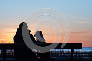 Womana and dog sitting on bench near sunset seacoast