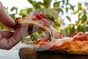 A woman`s fingers taking a slice of pizza from a wooden board close-up on nature blured background photo