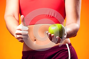 Womanin sportswear holding an apple and showing thumb up gesture. People, fitness and healthcare concept