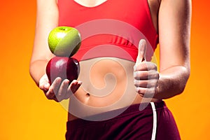 Womanin sportswear holding an apple and showing thumb up gesture. People, fitness and healthcare concept