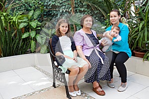 Womankind from infant, preteen girl, adult woman and senior grandmother, family in greenhouse on the bench