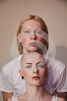 Womanly long haired man standing behind the bald masculine woman while posing