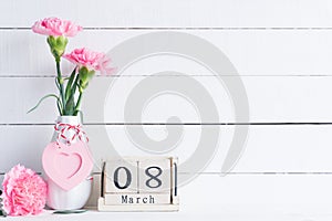 Womans day concept. Pink carnation flower in vase and red heart with March 8 text on wooden block calendar on white wooden