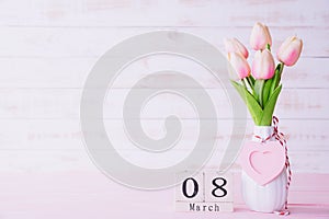 Womans day concept. Pink tulips and red heart with March 8 text on wooden block calendar on white wooden background