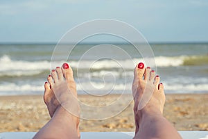 Womans feet on the beach. Female legs and feets with red nails on sunbed on the beach. Summer relaxation on sea background