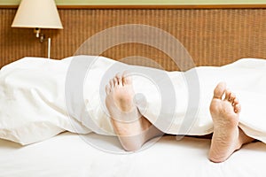 Womans Feet Sticking Out Of Blanket On Bed