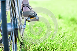 Womans foot on bicycle pedal on green grass closeup